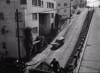 Movie still from “Dark Passage” (1947), directed by Delmer Daves – A man walking up a ramp next to a street; Extreme Wide shot, High angle