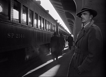 Movie still from “Dark Passage” (1947), directed by Delmer Daves – A black and white photo of a man standing in front of a train; Medium shot, Low angle