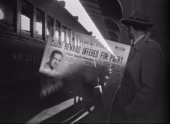 Movie still from “Dark Passage” (1947), directed by Delmer Daves – A man standing next to a train holding a newspaper; Medium shot, High angle