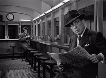 Movie still from “Dark Passage” (1947), directed by Delmer Daves – A man in a suit and a hat is reading a newspaper; Medium shot, High angle