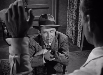 Movie still from “Dark Passage” (1947), directed by Delmer Daves – A man wearing a hat sitting in front of another man holding a gun; Medium shot, Over the shoulder angle
