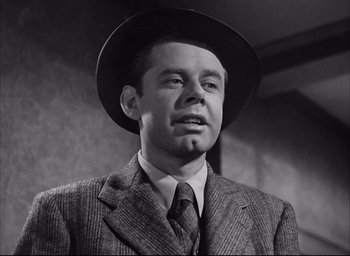 Movie still from “Dark Passage” (1947), directed by Delmer Daves – A man wearing a suit and a hat in a black and white photo; Close Up shot, Low angle