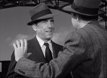 Movie still from “Dark Passage” (1947), directed by Delmer Daves – A man in a suit and a hat shaking another man's hand; Medium shot, Over the shoulder angle