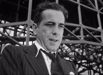 Movie still from “Dark Passage” (1947), directed by Delmer Daves – A man wearing a suit and tie standing in front of a metal structure; Close Up shot, Low angle