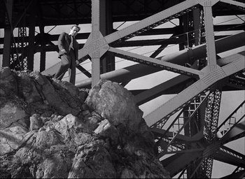 Movie still from “Dark Passage” (1947), directed by Delmer Daves – A man in a suit and tie walking on a bridge; Extreme Wide shot, Low angle