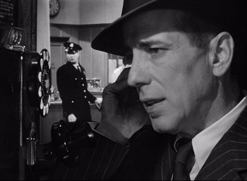 Movie still from “Dark Passage” (1947), directed by Delmer Daves – A man in a suit and hat talking on a phone; Close Up shot, Over the shoulder angle