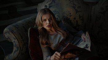 Movie still from “Dark Shadows” (2012), directed by Tim Burton – A woman sitting on top of a couch reading a book; Medium shot, High angle