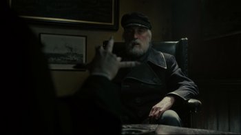 Movie still from “Dark Shadows” (2012), directed by Tim Burton – An older man sitting in a chair with a cigarette in his mouth; Medium shot, Over the shoulder angle