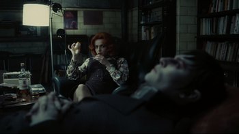 Movie still from “Dark Shadows” (2012), directed by Tim Burton – A woman sitting in a chair with a man laying on the couch; Medium shot, Low angle