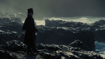 Movie still from “Dark Shadows” (2012), directed by Tim Burton – A man in a black coat and a black hat is standing on a rocky cliff; Wide shot, Low angle