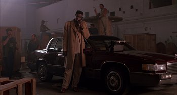 Movie still from “Darkman” (1990), directed by Sam Raimi – A man standing next to a car in a garage; Wide shot, Low angle