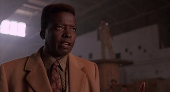 Movie still from “Darkman” (1990), directed by Sam Raimi – A man wearing a suit and tie standing in front of a building; Close Up shot, Low angle