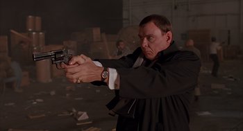 Movie still from “Darkman” (1990), directed by Sam Raimi – A man holding a gun while wearing a suit and tie; Medium shot, Low angle