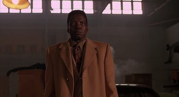 Movie still from “Darkman” (1990), directed by Sam Raimi – A man in a suit and tie standing in front of a building; Medium shot, Low angle