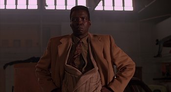 Movie still from “Darkman” (1990), directed by Sam Raimi – A man in a suit and tie standing in front of a window; Medium shot, Low angle