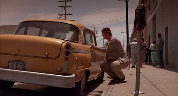 Movie still from “Darkman” (1990), directed by Sam Raimi – A man kneeling down next to an old yellow taxi cab; Wide shot, Low angle