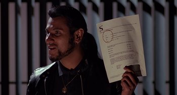 Movie still from “Darkman” (1990), directed by Sam Raimi – A man holding up a piece of paper with a circle on it; Close Up shot, Over the shoulder angle