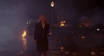 Movie still from “Darkman” (1990), directed by Sam Raimi – A woman is standing in front of a car on fire; Wide shot, Low angle