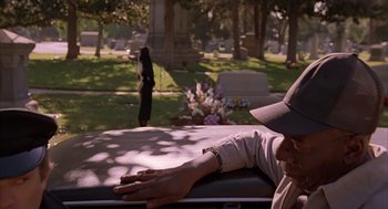 Movie still from “Darkman” (1990), directed by Sam Raimi – A man laying on a bench in a cemetery; Medium shot, Over the shoulder angle