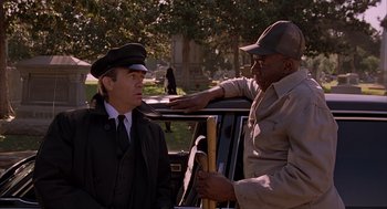 Movie still from “Darkman” (1990), directed by Sam Raimi – Two men in hats are standing next to a car; Medium shot, Over the shoulder angle