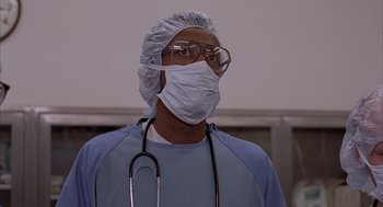 Movie still from “Darkman” (1990), directed by Sam Raimi – A man wearing a surgical mask with a stethoscope around his neck; Close Up shot, Low angle