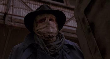Movie still from “Darkman” (1990), directed by Sam Raimi – A man in a hat and a trench coat with bandages on his face; Close Up shot, Low angle