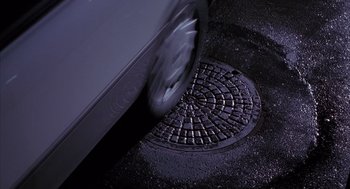 Movie still from “Darkman” (1990), directed by Sam Raimi – A manhole cover on the side of the street; Wide shot, Overhead angle