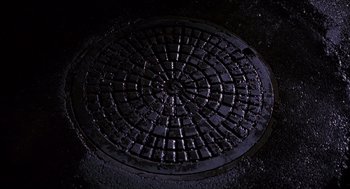 Movie still from “Darkman” (1990), directed by Sam Raimi – A manhole cover in the middle of the night; Extreme Close Up shot, Overhead angle