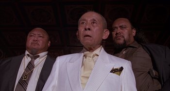 Movie still from “Darkman” (1990), directed by Sam Raimi – A group of men standing next to each other in a room; Medium shot, Low angle