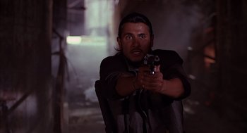 Movie still from “Darkman” (1990), directed by Sam Raimi – A man holding a gun while standing in a dark room; Close Up shot, Low angle