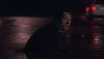 Movie still from “Darkman III: Die Darkman Die” (1996), directed by Bradford May – A man sitting on the ground in the dark; Medium shot, High angle