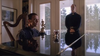 Movie still from “Darkman III: Die Darkman Die” (1996), directed by Bradford May – A man sitting at a dining room table in front of a mirror; Medium shot, Low angle