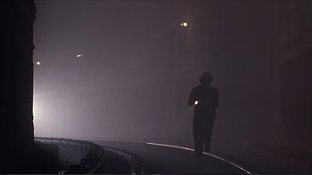 Movie still from “Darkman III: Die Darkman Die” (1996), directed by Bradford May – A person is standing in the fog holding a flashlight; Extreme Wide shot, Low angle