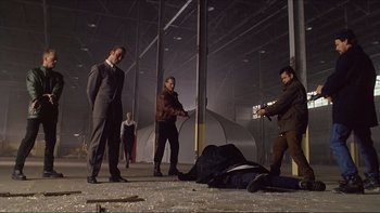 Movie still from “Darkman III: Die Darkman Die” (1996), directed by Bradford May – A group of men standing around a body covered in rain; Wide shot, Low angle
