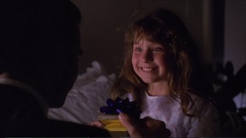 Movie still from “Darkman III: Die Darkman Die” (1996), directed by Bradford May – A little girl smiles as she holds a present; Close Up shot, Over the shoulder angle
