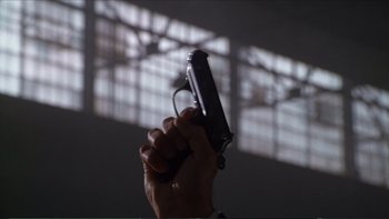 Movie still from “Darkman III: Die Darkman Die” (1996), directed by Bradford May – A person holding a gun in their hand; Extreme Close Up shot, Low angle