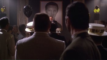 Movie still from “Darkman III: Die Darkman Die” (1996), directed by Bradford May – Two men are listening to a speaker in front of a portrait of a man; Medium shot, Over the shoulder angle