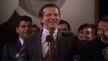Movie still from “Darkman III: Die Darkman Die” (1996), directed by Bradford May – A man in a suit and tie standing in front of a microphone; Medium shot, Low angle