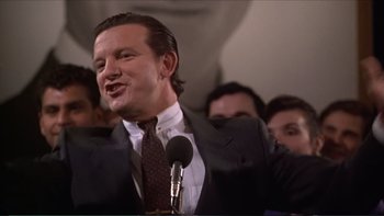 Movie still from “Darkman III: Die Darkman Die” (1996), directed by Bradford May – A man in a suit and tie speaking into a microphone; Close Up shot, Low angle