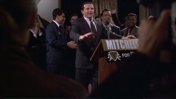 Movie still from “Darkman III: Die Darkman Die” (1996), directed by Bradford May – A man in a suit and tie speaking at a podium; Medium shot, High angle