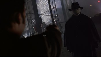 Movie still from “Darkman III: Die Darkman Die” (1996), directed by Bradford May – A man in a black coat and a black hat; Medium shot, Over the shoulder angle