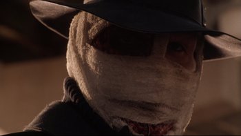 Movie still from “Darkman II: The Return of Durant” (1995), directed by Bradford May – A man with a mask and a hat on; Close Up shot, Over the shoulder angle