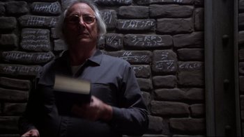 Movie still from “Darkman II: The Return of Durant” (1995), directed by Bradford May – A man holding a book standing in front of a brick wall; Medium shot, Low angle
