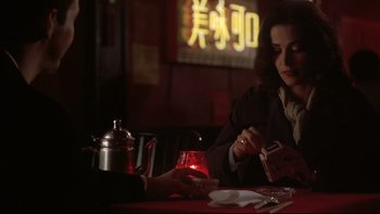 Movie still from “Darkman II: The Return of Durant” (1995), directed by Bradford May – A woman sitting at a table in front of a tea pot; Medium shot, Over the shoulder angle