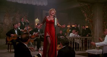 Movie still from “Das Boot” (1981), directed by Wolfgang Petersen – A woman in a long red dress singing into a microphone; Wide shot, Low angle