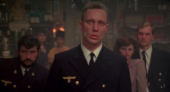 Movie still from “Das Boot” (1981), directed by Wolfgang Petersen – A man in a suit and tie standing in front of a group of people; Close Up shot, Over the shoulder angle