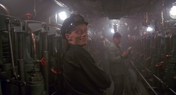 Movie still from “Das Boot” (1981), directed by Wolfgang Petersen – A man wearing a hat in a room with other men; Medium shot, High angle