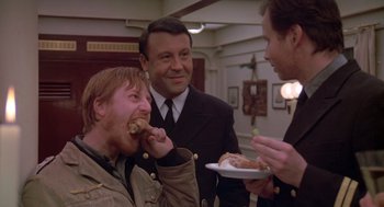 Movie still from “Das Boot” (1981), directed by Wolfgang Petersen – A group of men standing next to each other eating food; Medium shot, Over the shoulder angle