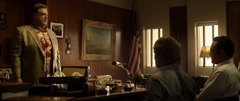 Movie still from “The Internship” (2013), directed by Shawn Levy – A man sitting at a desk in front of an american flag; Wide shot, Low angle
