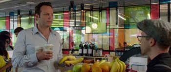 Movie still from “The Internship” (2013), directed by Shawn Levy – A man standing in front of a counter holding bananas; Medium shot, Over the shoulder angle